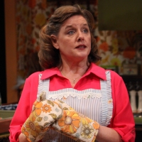 Woman in a pink dress and apron wearing oven mits
