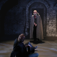 A man in a cap looming over a man on the ground with his hands up protecting himself