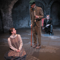 A woman on the ground with a man standing over her speaking down to her, another man observes from behind them