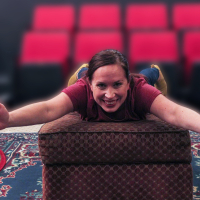 A woman laying on her belly on an ottoman looking at the camera and smiling
