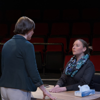 A woman sitting at a desk looking up at another woman facing her