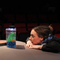 A woman looking into a tank with a goldfish in it