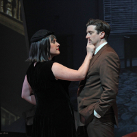 A woman dressed in black putting her finger on a man's mouth to stop him from speaking