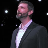 One man in a suit with a beard looking up into the distance to the left