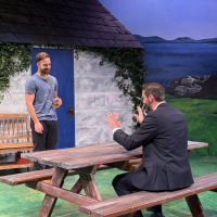 One man sitting at a picnic table and another standing across from him holding a coffee cup
