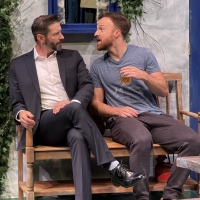 Two bearded men sitting next to each other on a bench, one on the right leaning into the one on the left