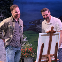 Two bearded men standing and looking at a painting on an easle