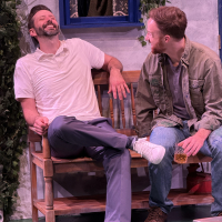Two men sitting on a bench, one on the left laughing at the one ont the right who is looking at him