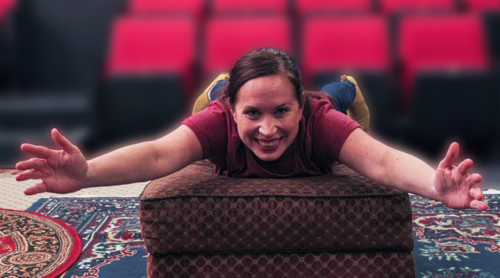 A woman laying on her belly on an ottoman looking at the camera and smiling