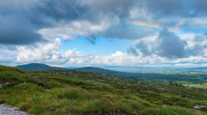 Photo of the rolling Irish hills with a rainbow in the sky